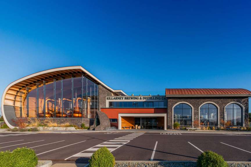 Das Bild zeigt das Killarney Brewing & Distilling Co. Gebäude mit seiner markanten Architektur und den großen Kupferdestillierkolben im Glasanbau.