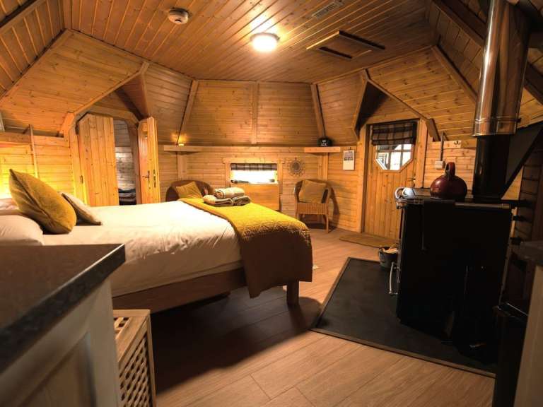 Das Bild zeigt ein gemütliches Schlafzimmer mit Holzwänden und einer Eckbank vor einem Ofen.
