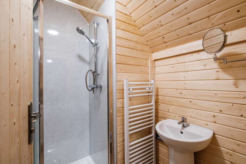 Ein Badezimmer mit Holzwänden und einer Duschkabine ist mit einem Waschbecken, einem Handtuchwärmer und einem Spiegel ausgestattet.