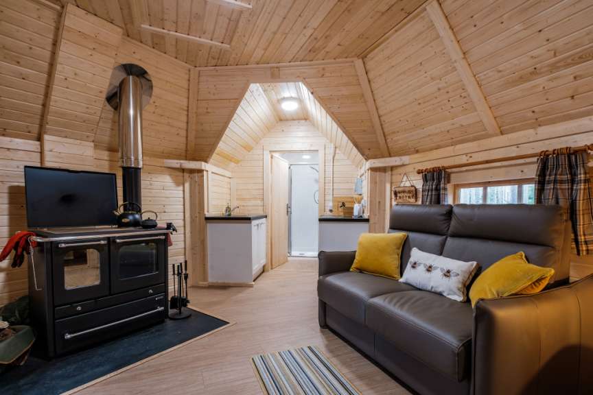 Ein gemütliches Holzhaus mit Wohnbereich, Küche und einer Dusche, beleuchtet durch eine Deckenlampe.