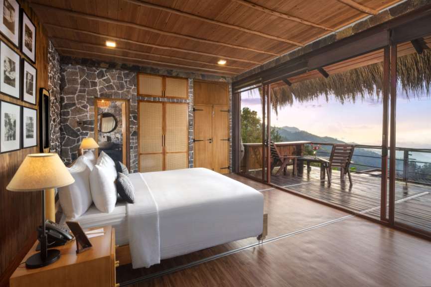 Ein Schlafzimmer mit Holzboden und Steinwand geht auf eine möblierte Terrasse mit Bergblick hinaus.