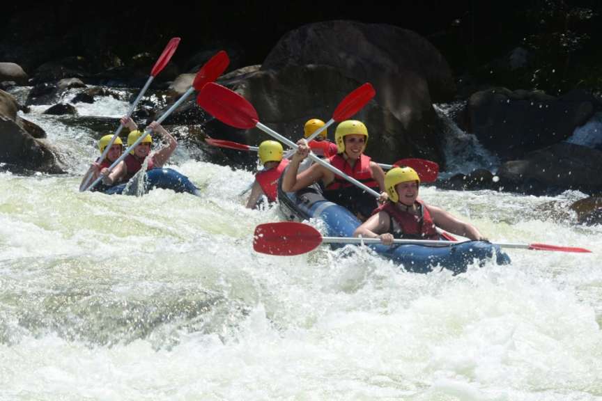 Eine Gruppe von Menschen in einem Schlauchboot fährt auf einem reißenden Fluss mit Paddeln.