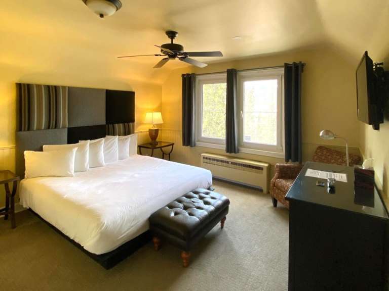 In dem Bild wird ein Hotelzimmer mit einem großen Bett, einem Schreibtisch und einem Fernseher gezeigt.