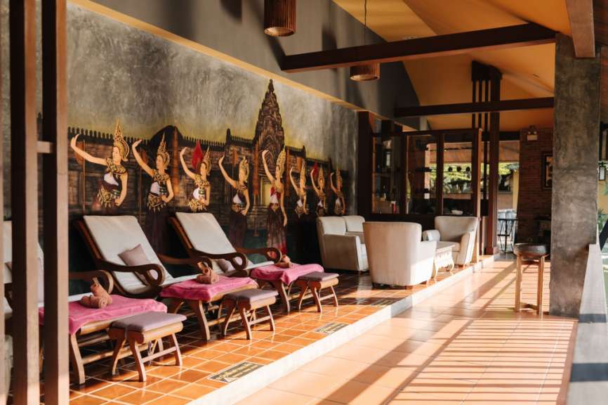Ein Wartebereich in einem Spa mit Liegestühlen, Sitzgelegenheiten und einer Wandmalerei mit Tänzerinnen.