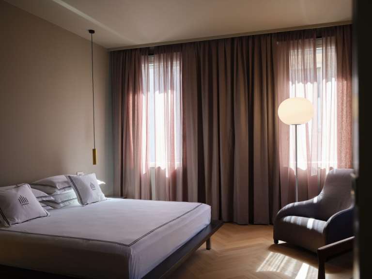 Ein modernes Schlafzimmer mit einem Bett, Vorhängen, einem Sessel und einer Stehlampe.