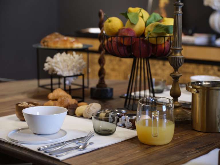 Ein Frühstückstisch mit Croissants, Obst, Orangensaft und anderen Leckereien steht bereit.