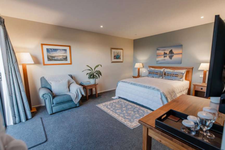 Das Bild zeigt ein gemütliches Schlafzimmer mit einem großen Bett, einem Sessel und einer schönen Landschaftsdarstellung an der Wand.