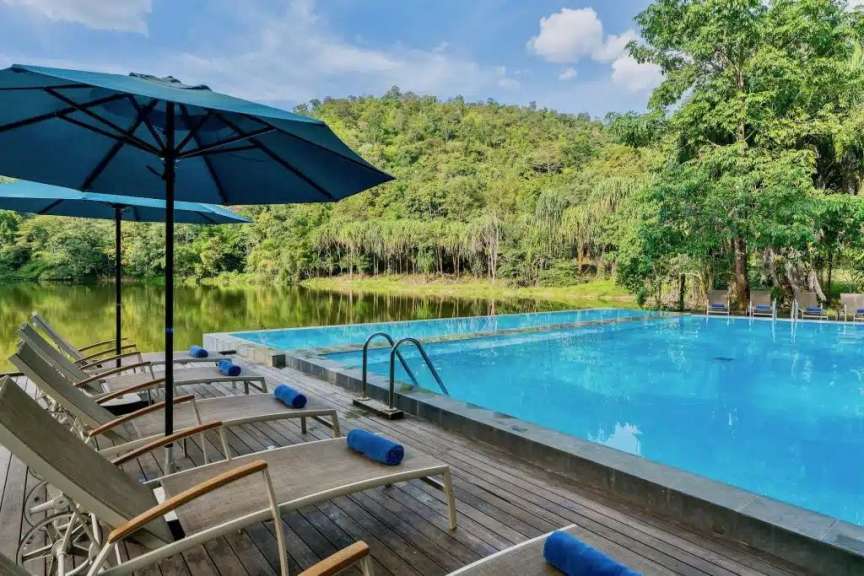 Ein luxuriöser Infinity-Pool mit Liegestühlen und Sonnenschirmen blickt auf einen ruhigen See und einen üppigen Wald.
