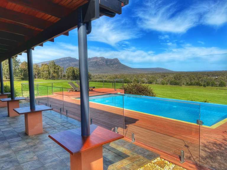 Ein Pool mit Holzterrasse und Blick auf eine Berglandschaft an einem sonnigen Tag.