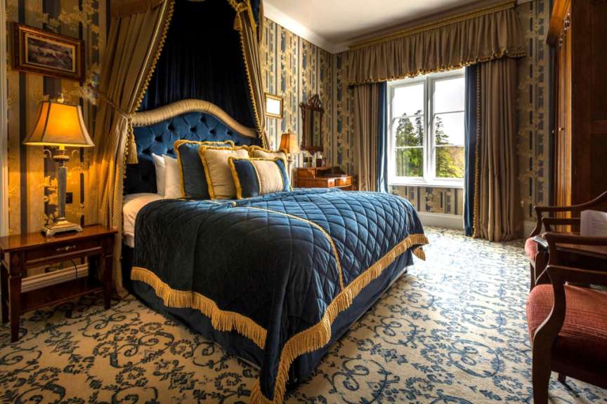 Ein luxuriöses Hotelzimmer mit einem Himmelbett, prunkvollen Vorhängen und einem gemusterten Teppich.