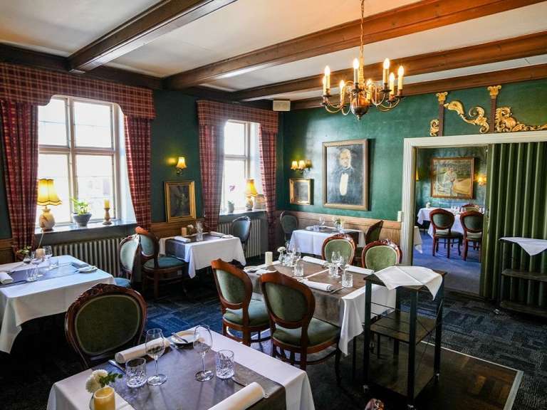 Ein geschmackvoll eingerichtetes Restaurant mit grünen Wänden, Holzbalken an der Decke und Tischen, die für Gäste gedeckt sind.