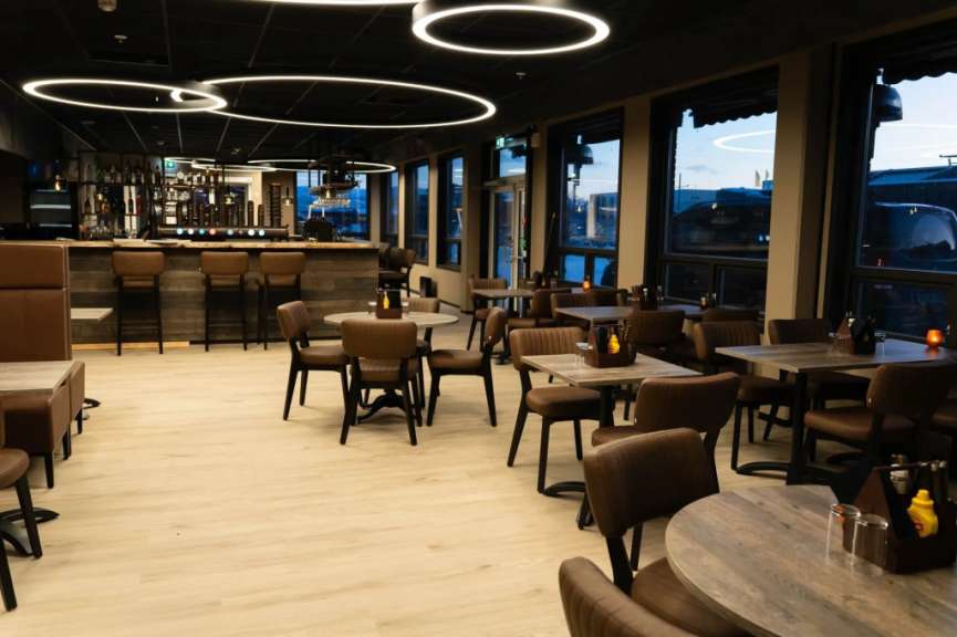 Dieses Bild zeigt ein Restaurant mit einer Bar, Tischen und Stühlen in einem modernen Ambiente.