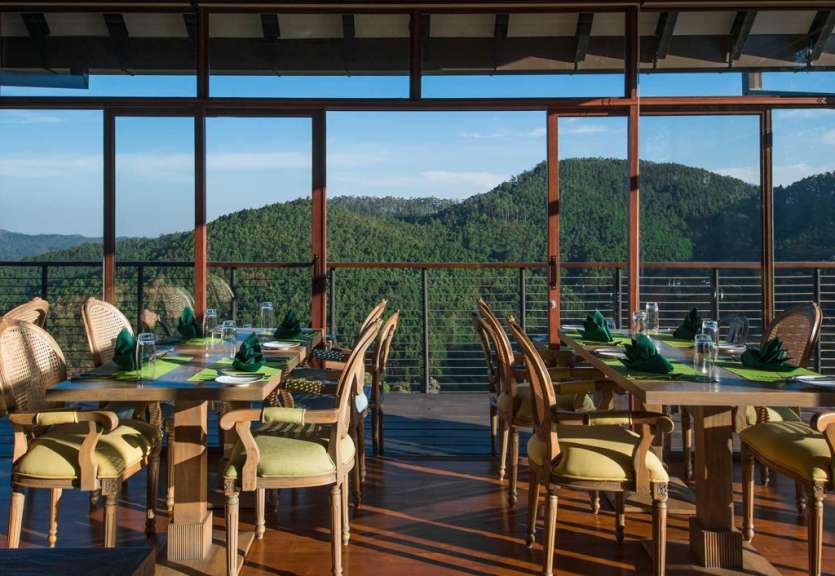Ein Restaurant mit Blick auf einen grünen Berg mit Holztischen und Stühlen ist zu sehen.