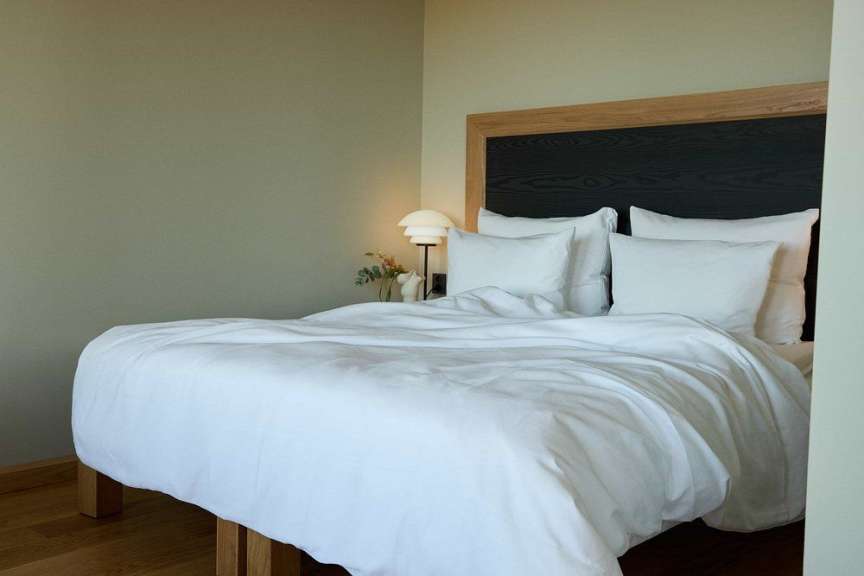 Ein Bett mit weißen Laken und Kissen steht vor einer grünen Wand und einem Holzkopfteil.