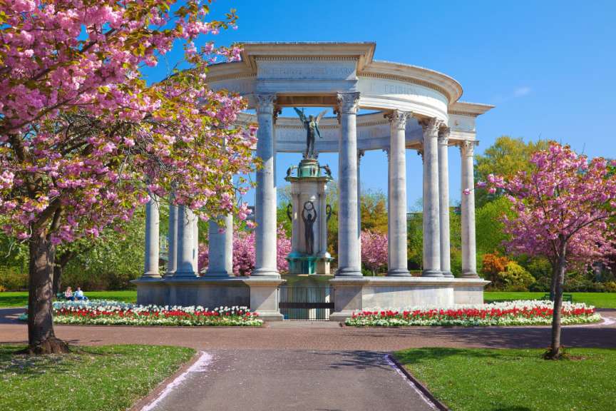 Eine Tempelanlage mit Säulen und einer Statue wird von blühenden Kirschbäumen und bunten Tulpen umrahmt.