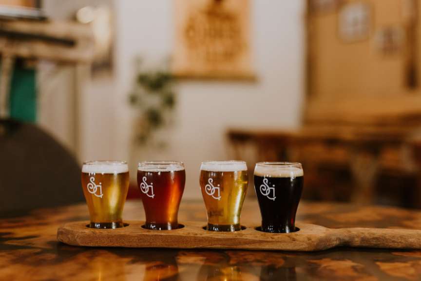 Vier Gläser Bier stehen auf einem Holztablett in einer Bar.