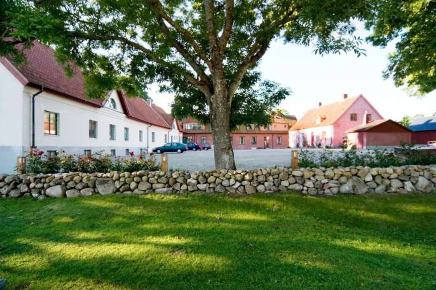 Ein Bauernhof mit mehreren Gebäuden, einem gepflasterten Hof und einem Steingarten mit grüner Wiese im Vordergrund.
