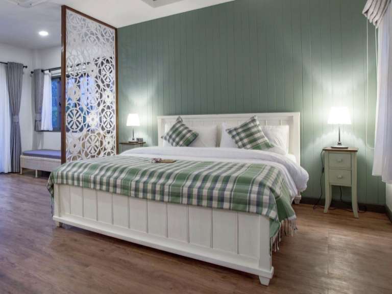 Ein Schlafzimmer mit einem weißen Bett, das mit einer grün karierten Decke und Kissen bedeckt ist, und einer holzverkleideten Wand in Salbeigrün.