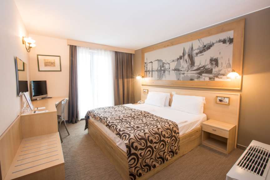 Ein gut beleuchtetes Hotelzimmer mit einem Doppelbett, Schreibtisch und Gemälde an der Wand.