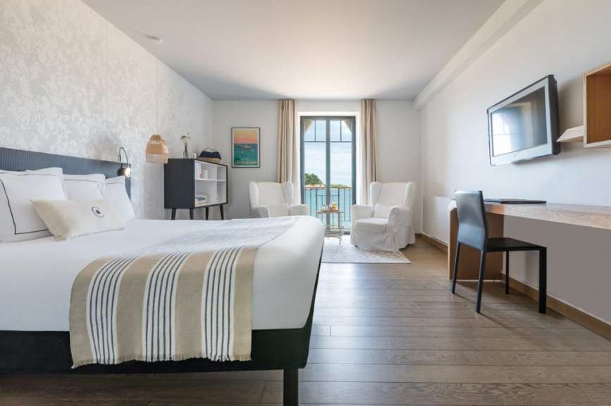 Ein stilvolles Hotelzimmer mit einem Bett, zwei Sesseln und einem Schreibtisch mit Blick aufs Meer.