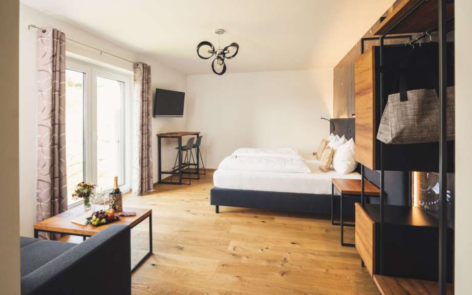 Ein modern eingerichtetes Schlafzimmer mit Holzboden, Doppelbett, Kleiderschrank und einem Sitzbereich am Fenster.