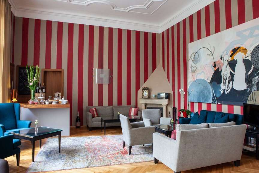 Ein großes Wohnzimmer mit rot-beiger Streifenwand, verschiedenen Sofas und Sesseln, einem Kamin und einem großen modernen Gemälde.