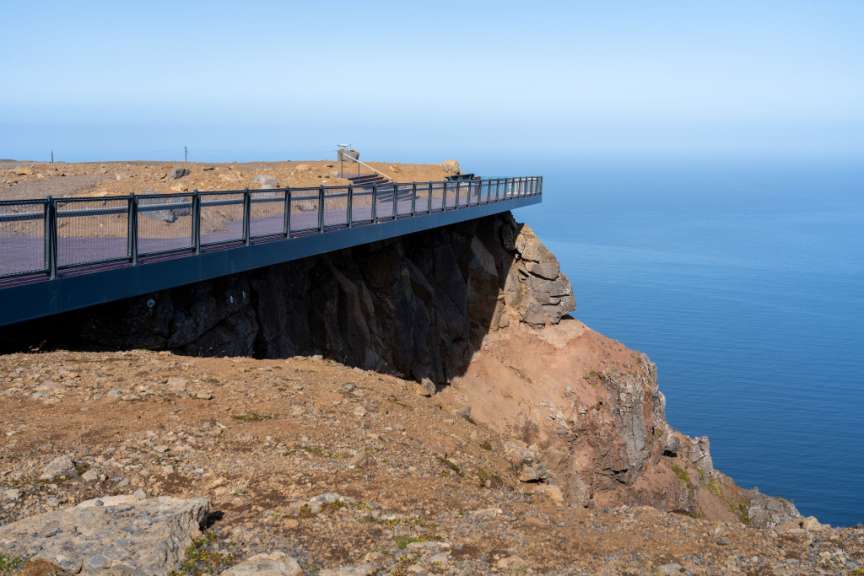 Ein Steg ragt über einen felsigen Abhang ins Meer hinaus.