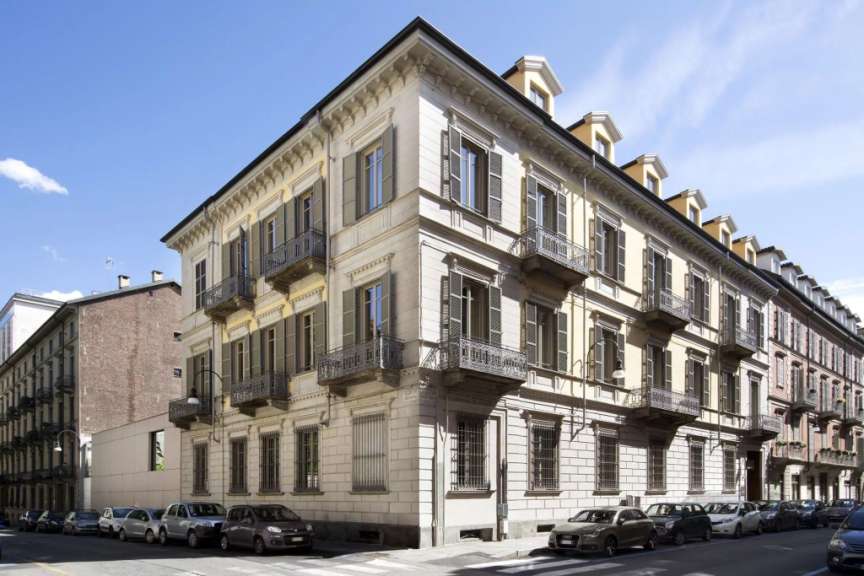 Das Bild zeigt eine belebte Straße mit Autos, die entlang einer Reihe von historischen Gebäuden mit Balkonen und Fensterläden geparkt sind.
