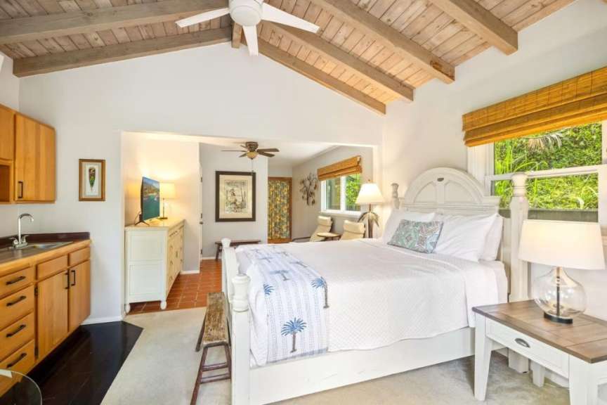 Ein Schlafzimmer mit einem weißen Bett, Holzbalken an der Decke und einer kleinen Küchenzeile.