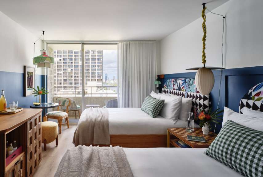 Zwei Betten mit gemusterten Kopfteilen stehen in einem modernen Hotelzimmer mit Blick auf eine Stadt.
