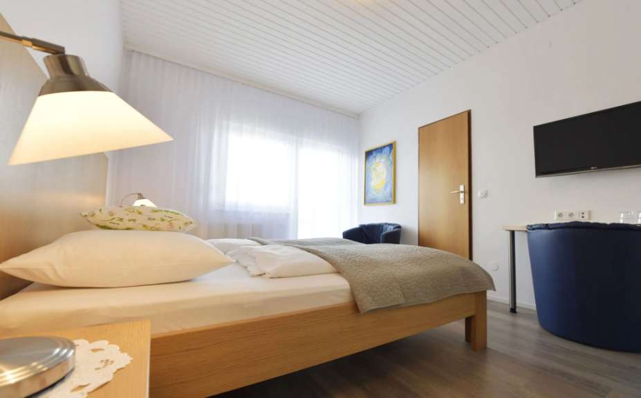 Ein Schlafzimmer mit einem Bett, Nachttisch, Schrank, einem Sessel und einem Fernseher an der Wand.