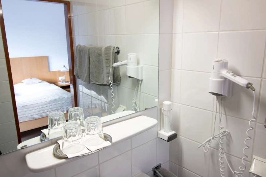 Ein Hotelzimmer mit einem Bett und einem Badezimmer mit Spiegel, Haartrockner und Gläsern.