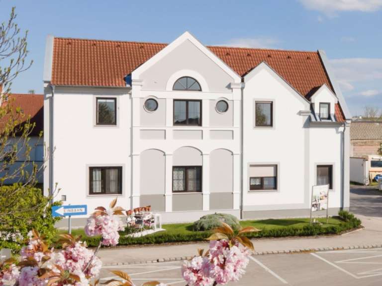 Ein dreistöckiges, weißes Gebäude mit roten Dachziegeln und mehreren Fenstern ist auf einer grünen Rasenfläche zu sehen.