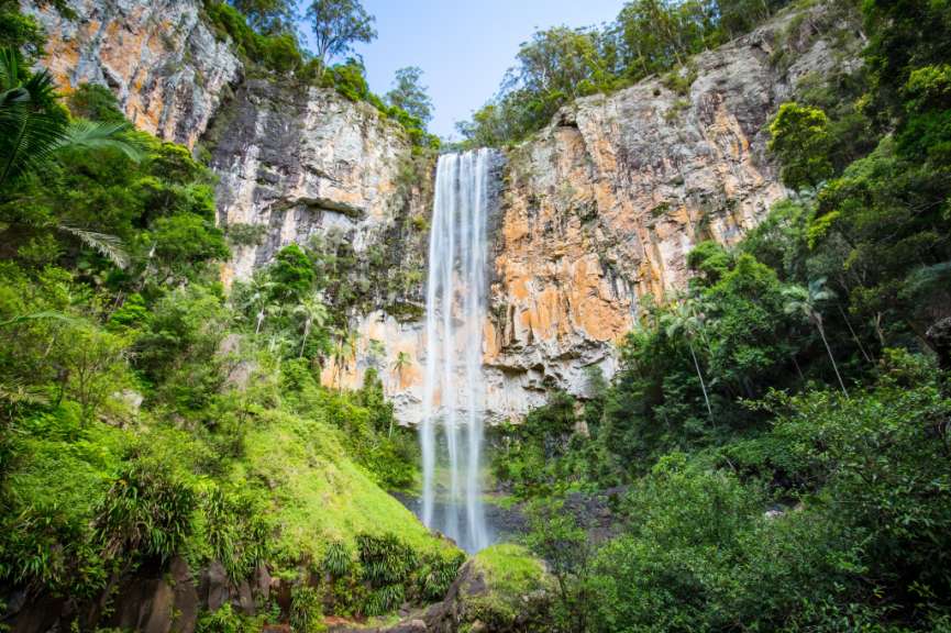 Ein beeindruckender Wasserfall stürzt von einer hohen, felsigen Klippe herab, die von üppigem Grün umgeben ist.