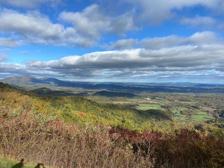 Ein Panoramablick aus der Höhe zeigt eine bergige Landschaft, die sich bis zum Horizont erstreckt, und den Himmel, der von Wolken durchzogen ist.