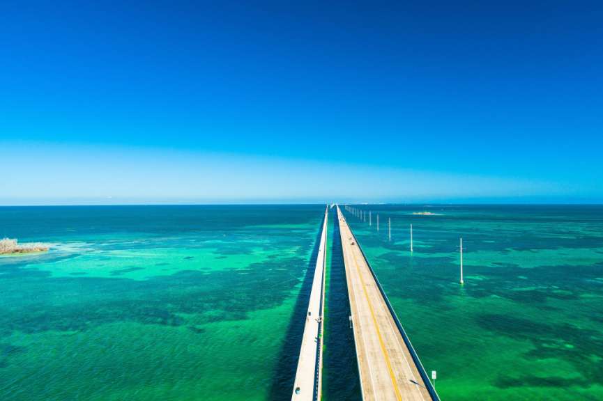 Eine lange Brücke führt über das türkisfarbene Meer unter einem strahlend blauen Himmel.