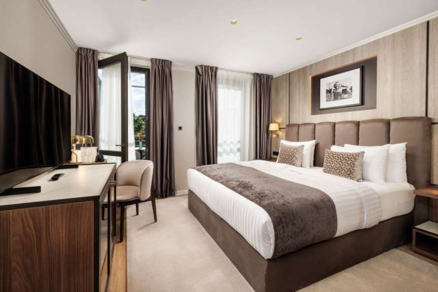 Ein großzügiges Schlafzimmer mit einem großen Bett, einem Schreibtisch, einem Fernseher und Zugang zu einem Balkon.