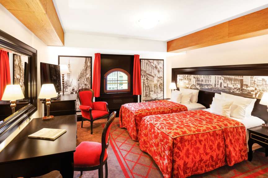 Ein Hotelzimmer mit zwei Betten, roten Akzenten und einem Schreibtisch.