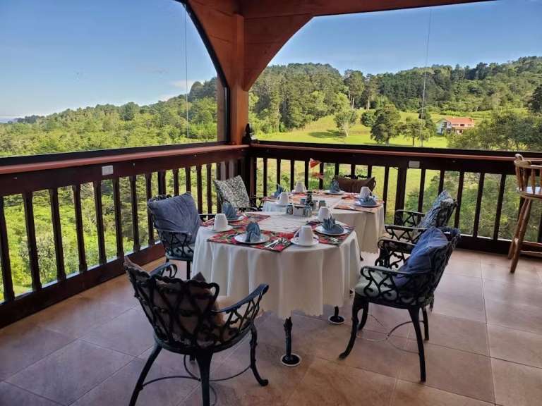 Ein gedeckter Tisch auf einer überdachten Terrasse mit Blick auf eine grüne Hügellandschaft.