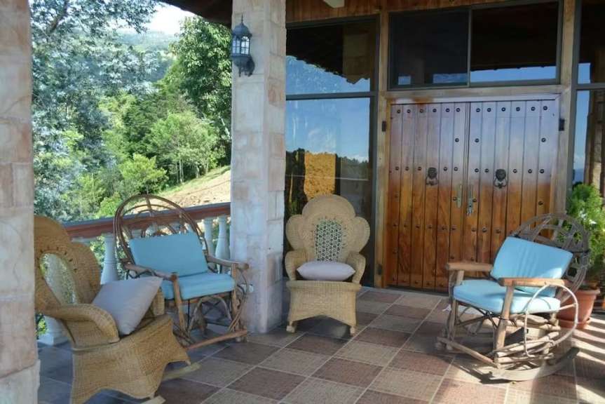 Eine möblierte Veranda mit Blick auf einen grünen Hügel mit vier Korbstühlen und Holztüren.