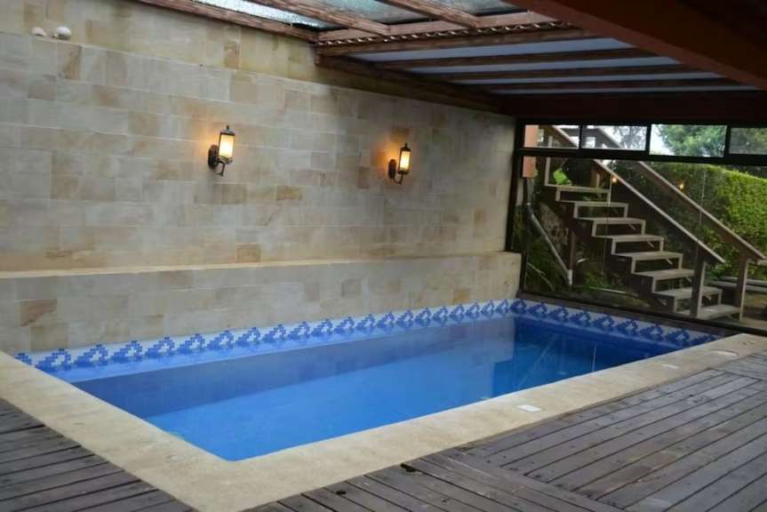 Ein kleiner Pool unter einem Holzdach mit Glaselementen, daneben Außentreppen.