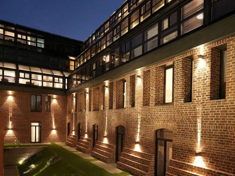 Ein Innenhof eines alten Ziegelgebäudes mit moderner Verglasung und Beleuchtung im Abendlicht.
