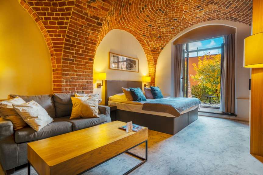 Ein Schlafzimmer mit Ziegelsteingewölbe und einer großen Tür, die auf einen kleinen Hof mit Bäumen und Tisch führt.