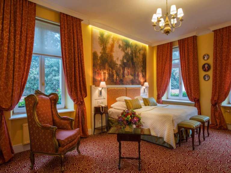 Ein luxuriöses Schlafzimmer mit einem großen Bett, einem verzierten Sessel und opulenten roten Vorhängen.
