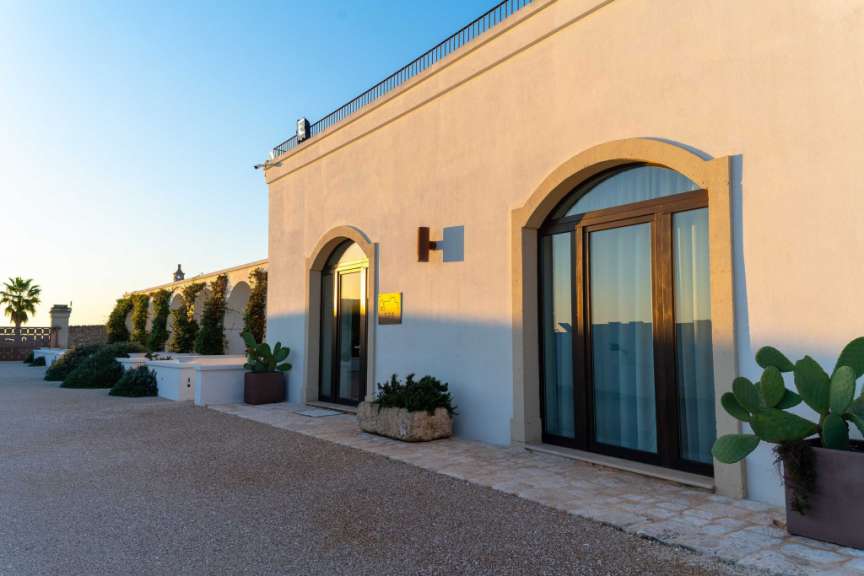 Eine moderne weiße Villa mit zwei Torbögen-Fenstern, einem "SPA"-Schild und einigen Kakteen.