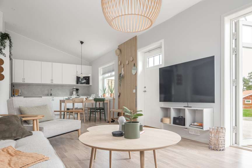 Ein modern eingerichtetes Wohnzimmer mit offener Küche, Esstisch und Sitzbereich, das durch ein großes Fenster viel Licht erhält.