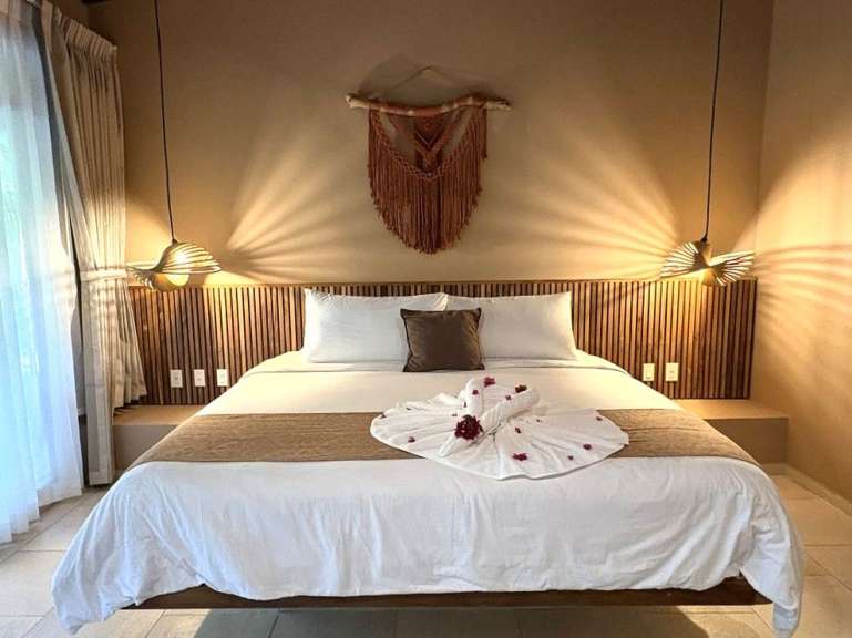 Ein gemütliches Schlafzimmer mit einem großen Bett, das mit weißen Bettwäsche, einem braunen Akzenttuch und gefalteten Handtüchern in Schwanenform dekoriert ist.