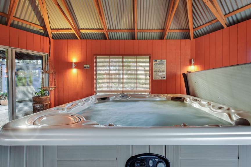 Ein Whirlpool ist in einem orangefarbenen Raum mit Wellblechdach und großen Fenstern zu sehen.