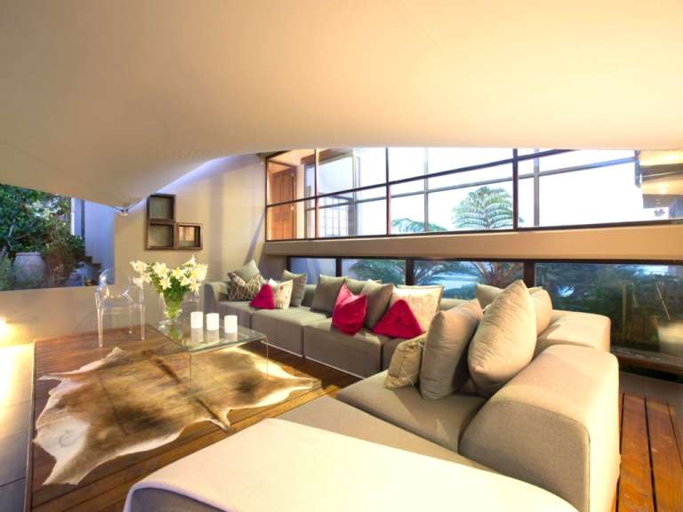 Dieses Bild zeigt ein Wohnzimmer mit einer Eckcouch, einem Couchtisch aus Glas und einer Kuhhaut als Teppich, mit Blick auf eine tropische Landschaft durch große Fenster.