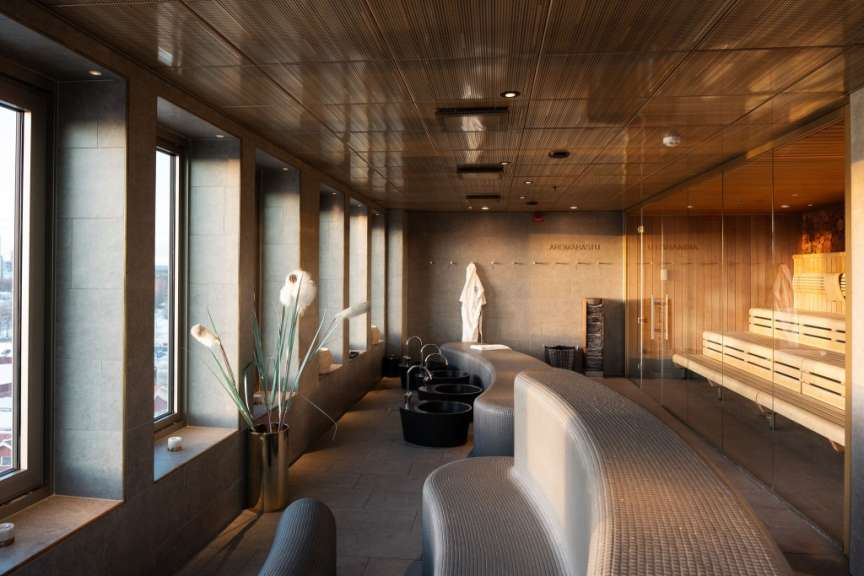 Ein moderner Spa-Bereich mit Fußwaschbecken, Ruhebänken und einer Glas-Sauna.